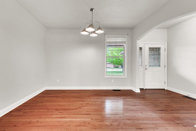 unfurnished room featuring a chandelier, wood finished floors, and baseboards
