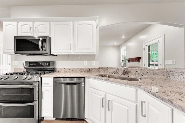 kitchen with a sink, stainless steel appliances, white cabinetry, light stone countertops, and arched walkways