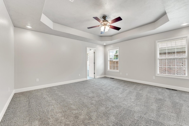 empty room featuring a raised ceiling, carpet flooring, baseboards, and a ceiling fan