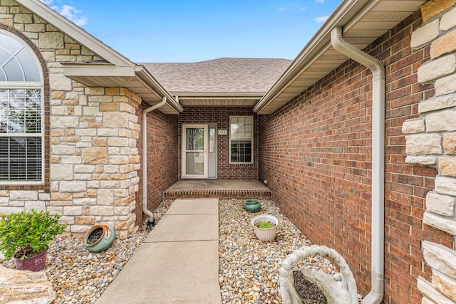 doorway to property featuring a shingled roof, stone siding, and brick siding