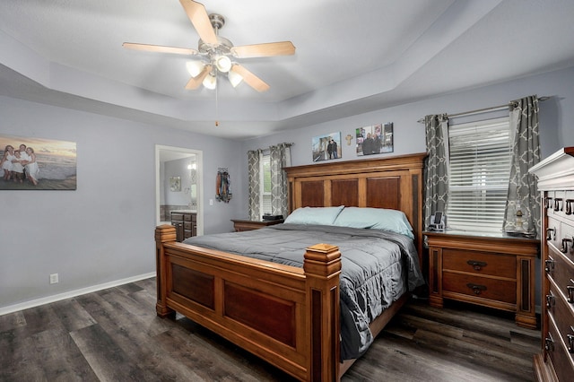 bedroom featuring dark wood finished floors, a ceiling fan, a raised ceiling, connected bathroom, and baseboards