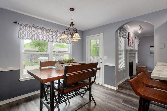 dining space featuring dark wood finished floors, a fireplace, arched walkways, a notable chandelier, and baseboards