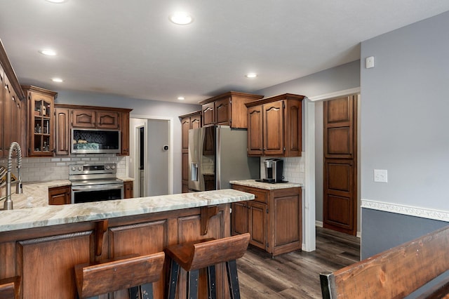 kitchen with glass insert cabinets, dark wood-style flooring, a peninsula, tasteful backsplash, and appliances with stainless steel finishes