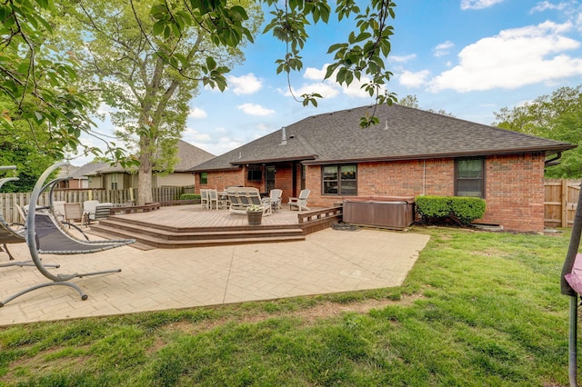 back of house with a hot tub, roof with shingles, brick siding, and fence