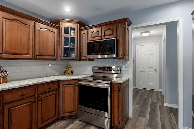 kitchen featuring stainless steel appliances, dark wood finished floors, backsplash, glass insert cabinets, and baseboards
