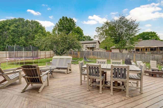 wooden terrace with a trampoline, outdoor dining area, a lawn, and a fenced backyard