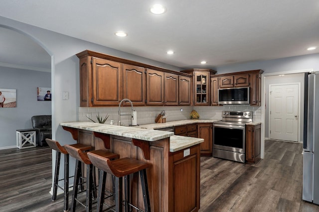 kitchen featuring a peninsula, backsplash, arched walkways, and appliances with stainless steel finishes