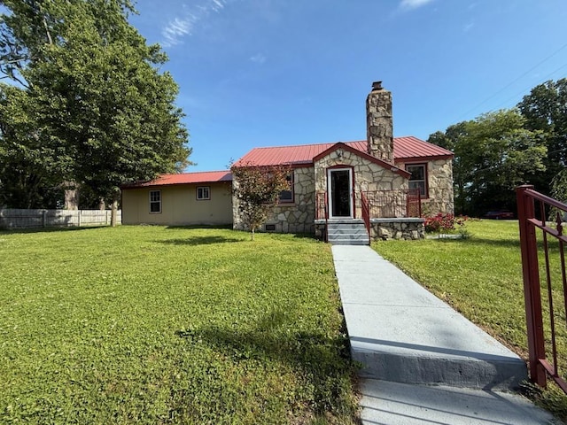 view of front of home with fence, stone siding, a front yard, metal roof, and a chimney