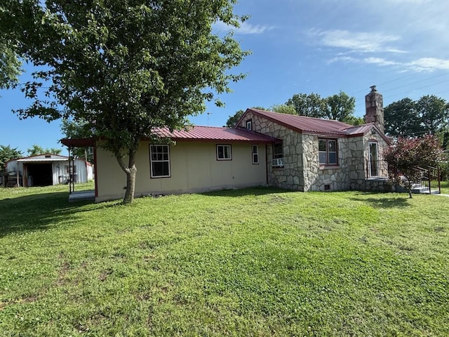 rear view of property with metal roof, stone siding, a chimney, and a lawn
