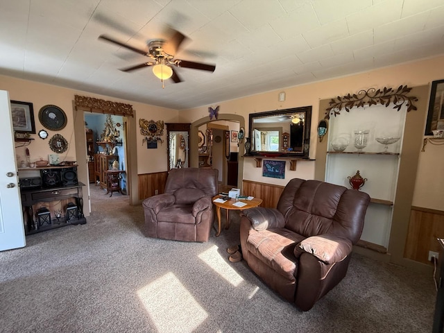 living room with a wainscoted wall, wood walls, ceiling fan, and carpet