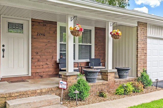view of exterior entry featuring covered porch, board and batten siding, brick siding, and a garage