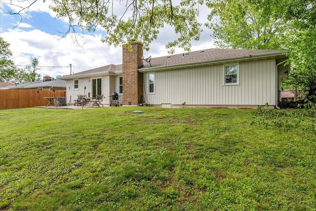 rear view of house featuring fence, a patio, a chimney, and a lawn