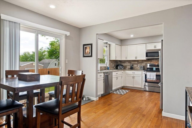 kitchen with light wood-style flooring, a sink, white cabinetry, backsplash, and appliances with stainless steel finishes