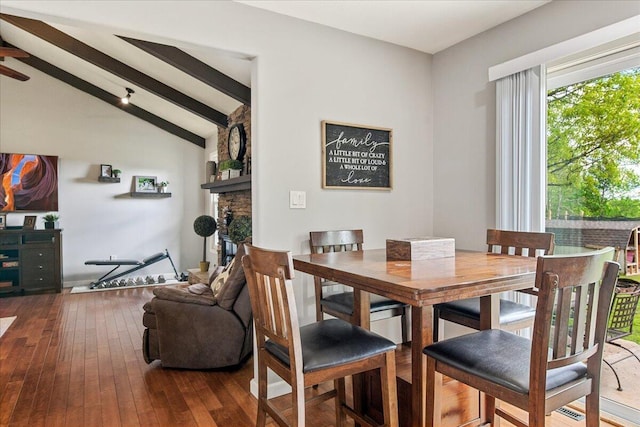 dining room with hardwood / wood-style floors, a stone fireplace, and vaulted ceiling with beams