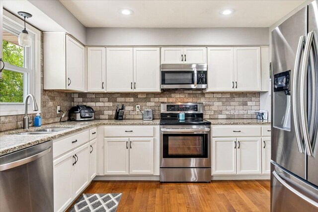 kitchen featuring a sink, light stone counters, light wood-type flooring, white cabinetry, and appliances with stainless steel finishes