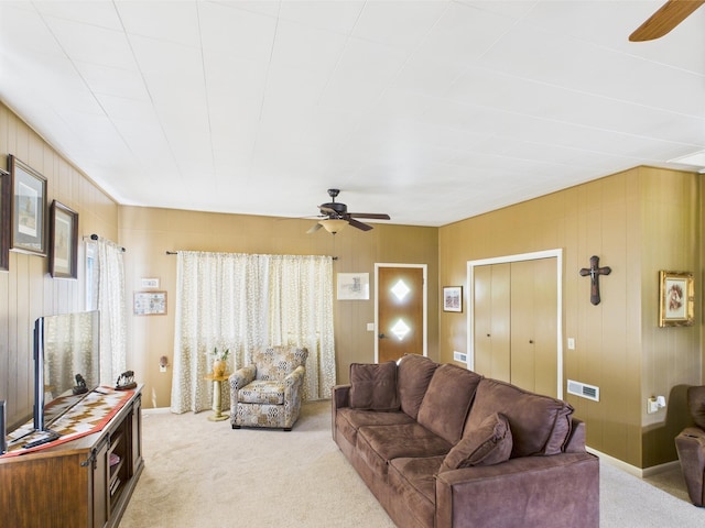 carpeted living room featuring wooden walls, visible vents, and ceiling fan