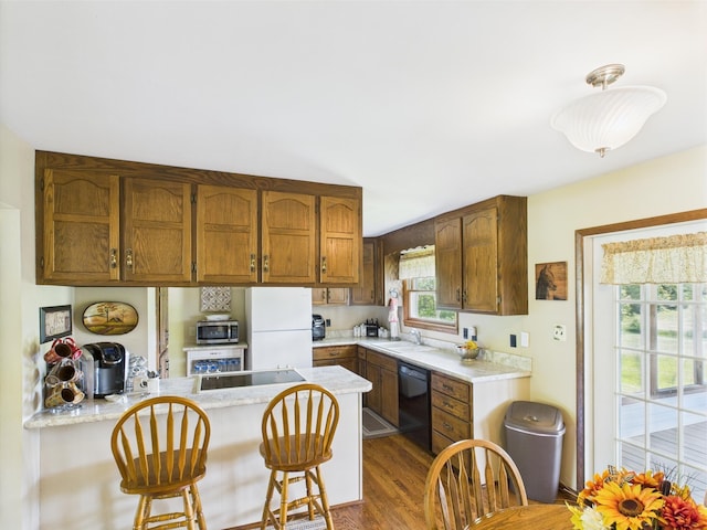 kitchen featuring a sink, a peninsula, wood finished floors, black appliances, and light countertops