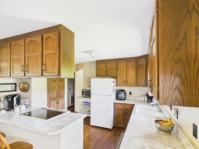 kitchen featuring a sink, a peninsula, stainless steel microwave, freestanding refrigerator, and black electric cooktop