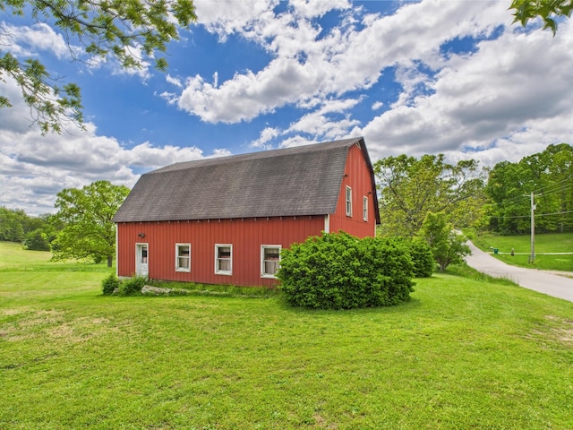 view of property exterior with roof with shingles, a gambrel roof, an outbuilding, a barn, and a lawn