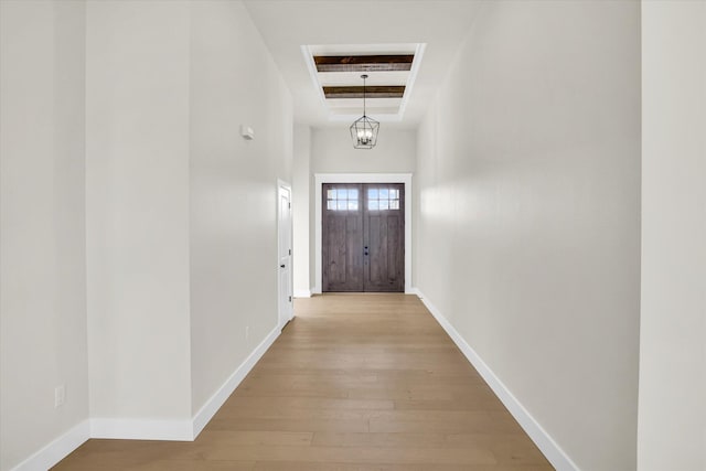 doorway to outside featuring light wood finished floors, a chandelier, baseboards, beam ceiling, and a high ceiling
