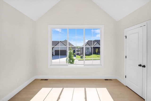 spare room featuring lofted ceiling, light wood finished floors, and baseboards