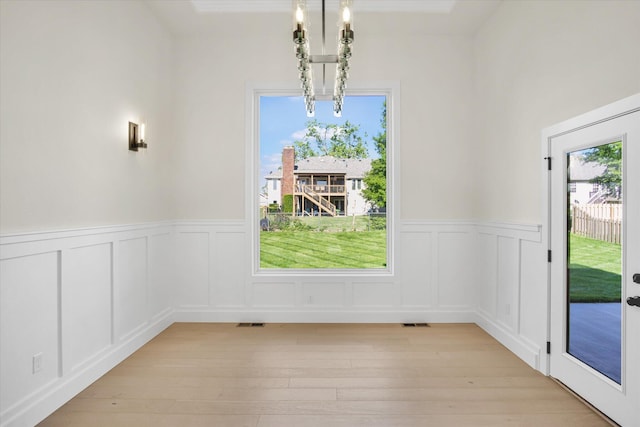 unfurnished dining area with a decorative wall, wainscoting, and light wood-type flooring