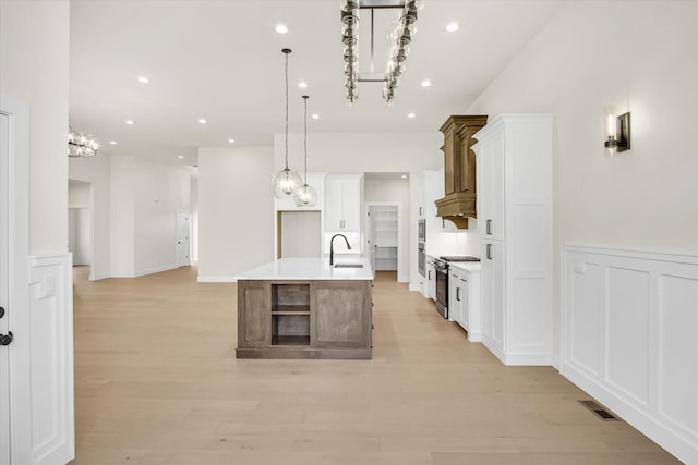 kitchen featuring stainless steel range with gas stovetop, a sink, white cabinetry, pendant lighting, and a wainscoted wall