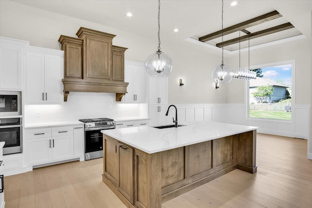kitchen featuring appliances with stainless steel finishes, a sink, light wood-style floors, wainscoting, and beamed ceiling