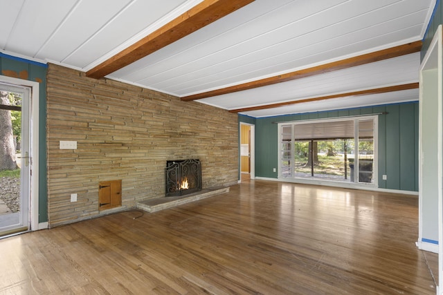 unfurnished living room featuring a stone fireplace, a healthy amount of sunlight, wood finished floors, and beamed ceiling