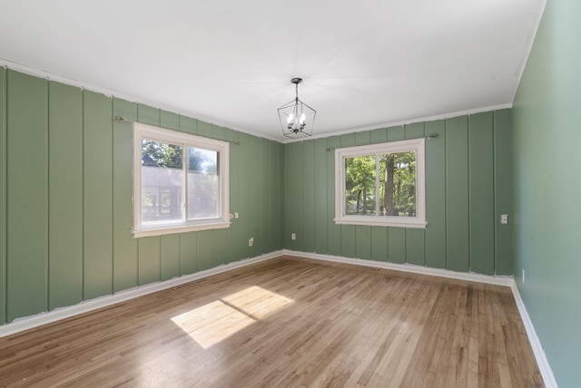unfurnished room with baseboards, a notable chandelier, ornamental molding, and wood finished floors