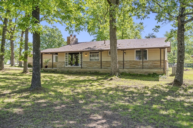 back of house featuring a yard, a chimney, and stone siding