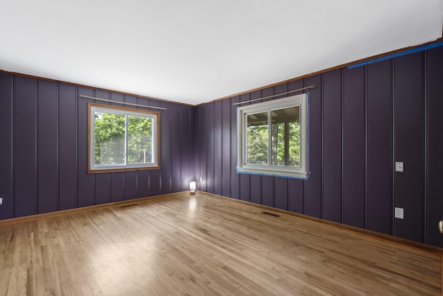 empty room with visible vents, a decorative wall, plenty of natural light, and wood finished floors