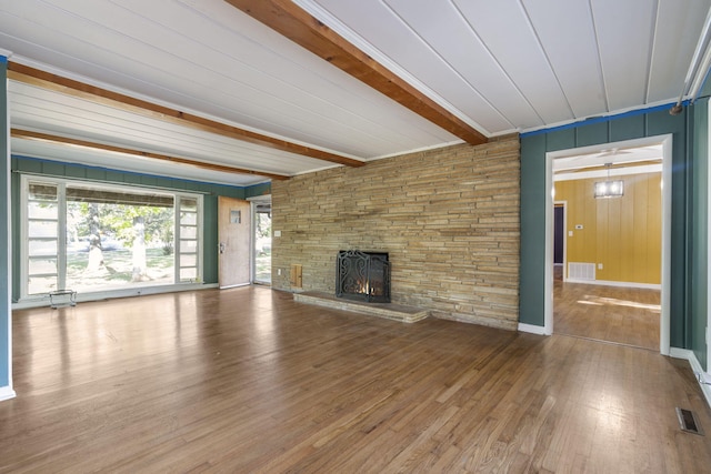 unfurnished living room featuring a fireplace, wood-type flooring, beamed ceiling, and visible vents