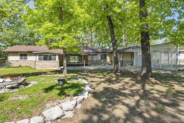 single story home with a front lawn, a chimney, a fire pit, and stone siding