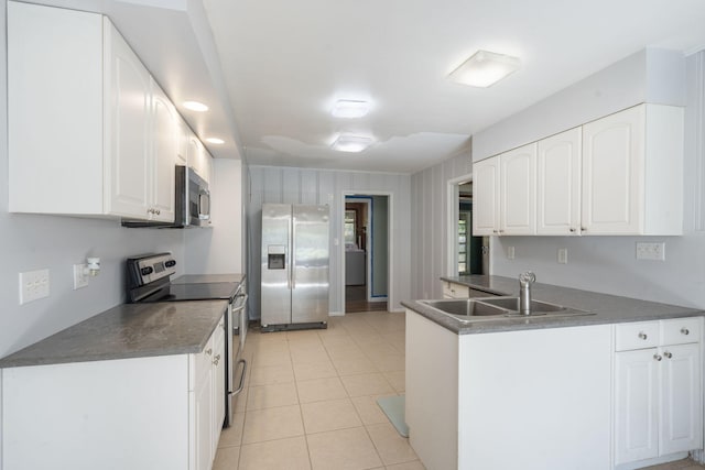 kitchen featuring a peninsula, a sink, dark countertops, stainless steel appliances, and white cabinets