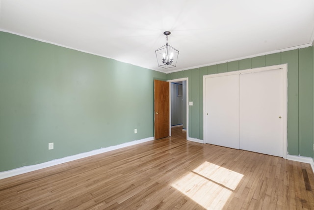 unfurnished bedroom featuring a closet, a chandelier, wood finished floors, and baseboards