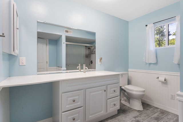 bathroom featuring toilet, a wainscoted wall, vanity, visible vents, and a shower stall