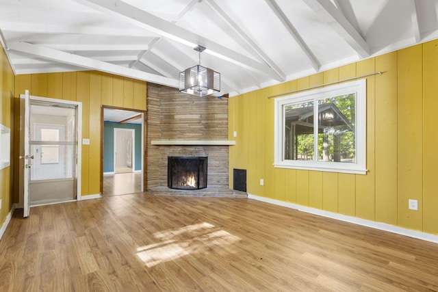 unfurnished living room with a fireplace, a notable chandelier, vaulted ceiling with beams, light wood-type flooring, and baseboards