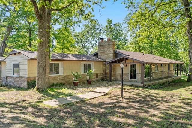back of property featuring stone siding, a chimney, and central AC