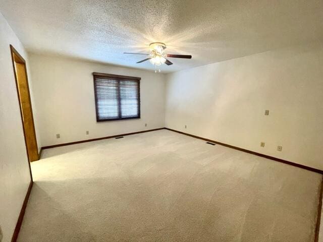 unfurnished room featuring light colored carpet, a textured ceiling, baseboards, and a ceiling fan