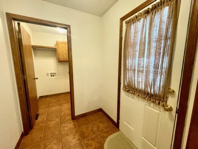 hall featuring a textured ceiling, dark tile patterned flooring, and baseboards