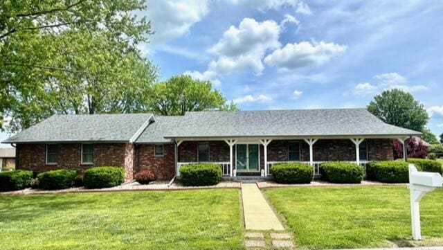 ranch-style house featuring covered porch, brick siding, and a front yard
