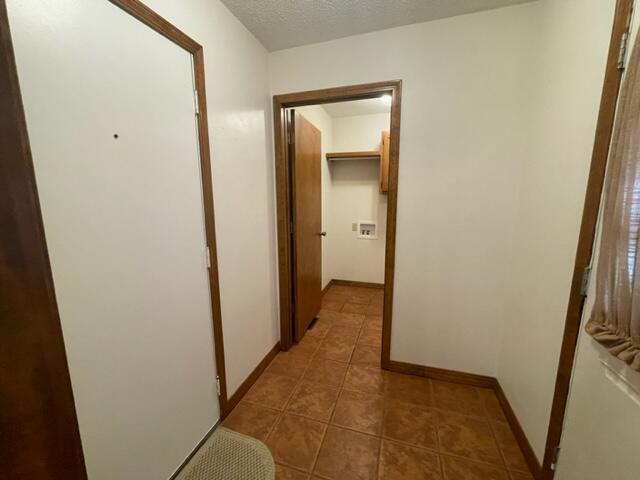corridor featuring baseboards, tile patterned flooring, and a textured ceiling