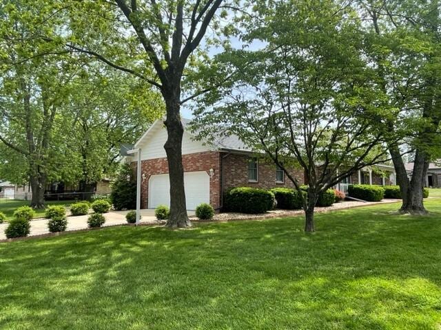 view of property exterior with an attached garage, concrete driveway, a yard, and brick siding