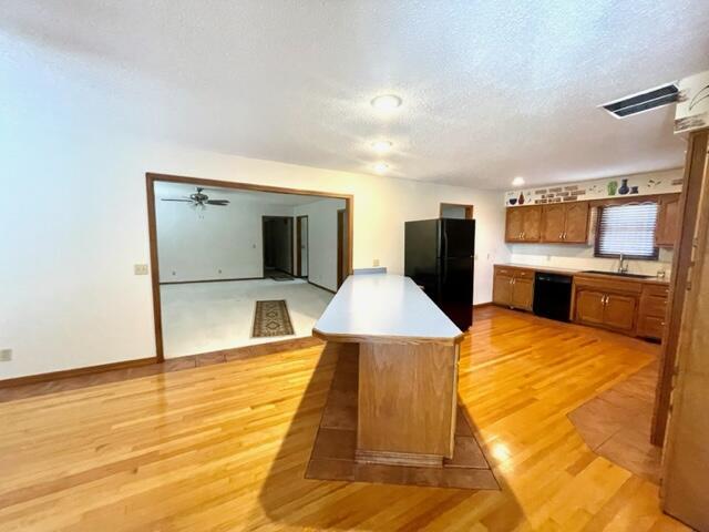kitchen featuring brown cabinets, a sink, black appliances, light countertops, and light wood-style floors