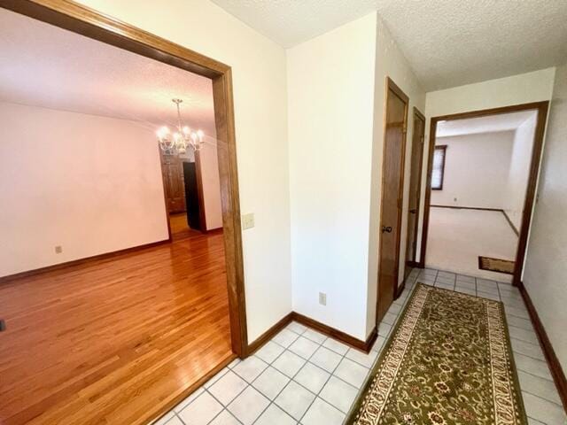 hall with an inviting chandelier, a textured ceiling, baseboards, and light tile patterned floors