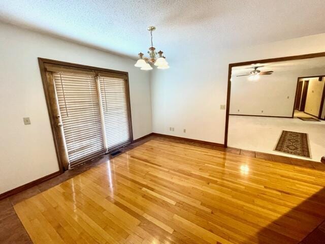 unfurnished room with wood finished floors, a notable chandelier, a textured ceiling, visible vents, and baseboards