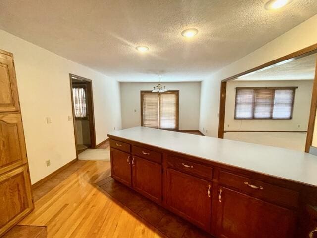 kitchen with a notable chandelier, a textured ceiling, baseboards, light countertops, and light wood-type flooring