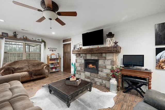 living room with wood finished floors, visible vents, a fireplace, and a ceiling fan