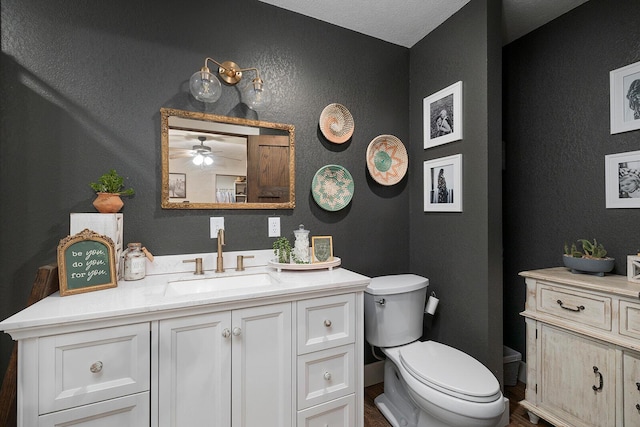 bathroom featuring a ceiling fan, toilet, vanity, and a textured wall